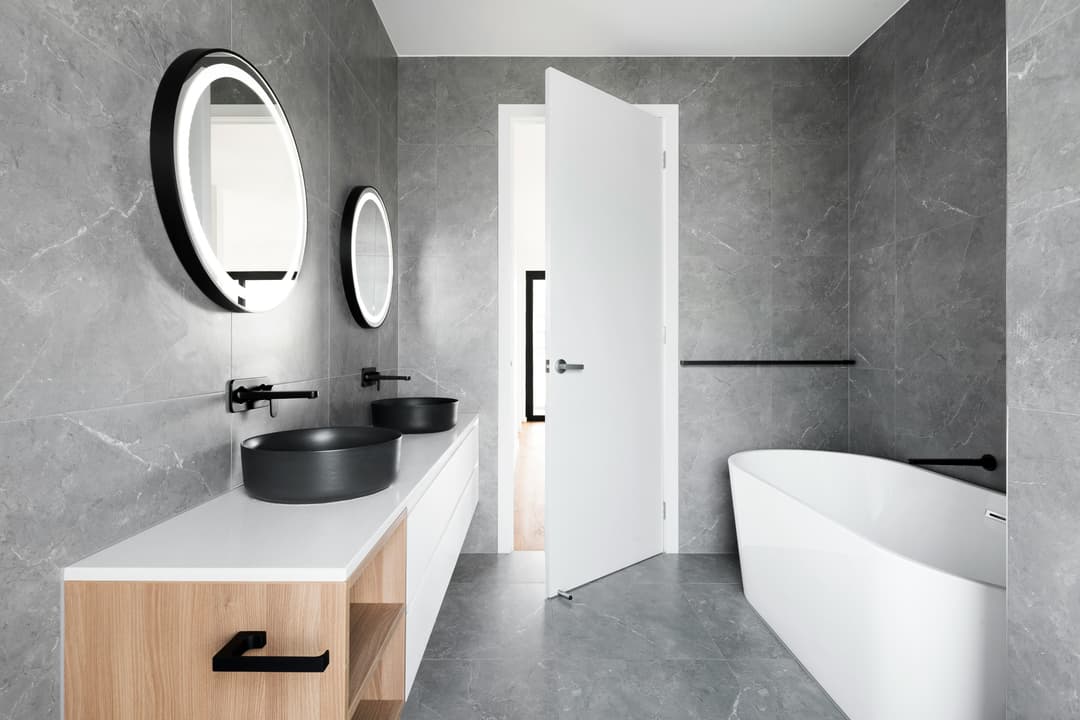 picture of a luxury bathroom with dual marble black sinks and gray tile and stonework on the floor and walls